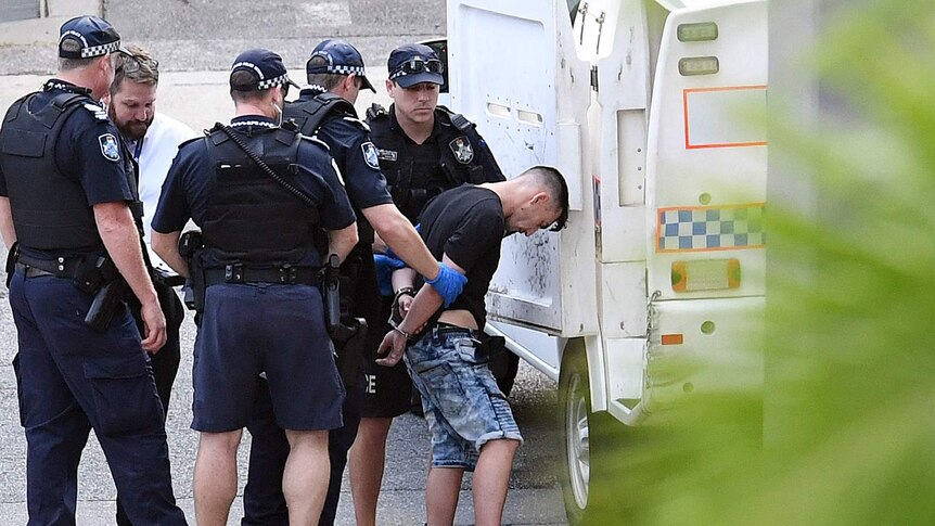 Man being taken into the back of the police wagon by police.