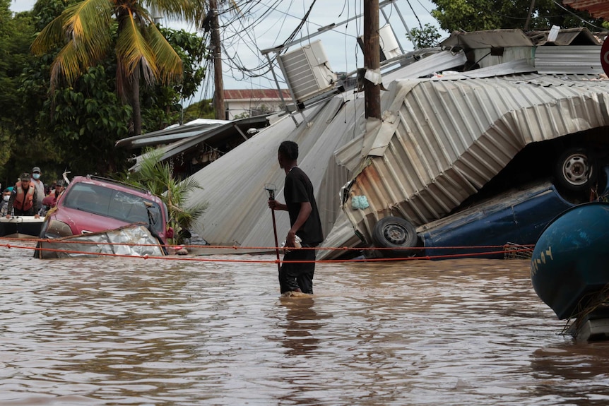 A resident walking through a flooded street looks back at storm damage.