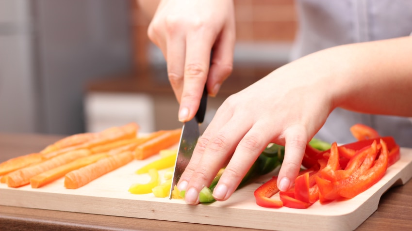 Woman cutting up different coloured capsicums on a wooden chopping block.