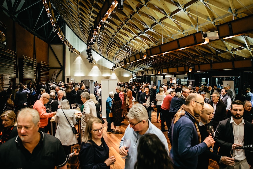 A crowded room - people standing in groups chatting while holding glasses of wine 