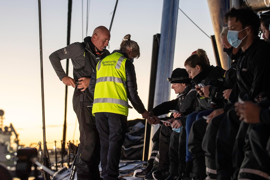 A biosecurity officer collects tests from a line of crew members.