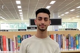 Bassam El Jamal smiles as he poses for a picture in a library wearing a white jumper 