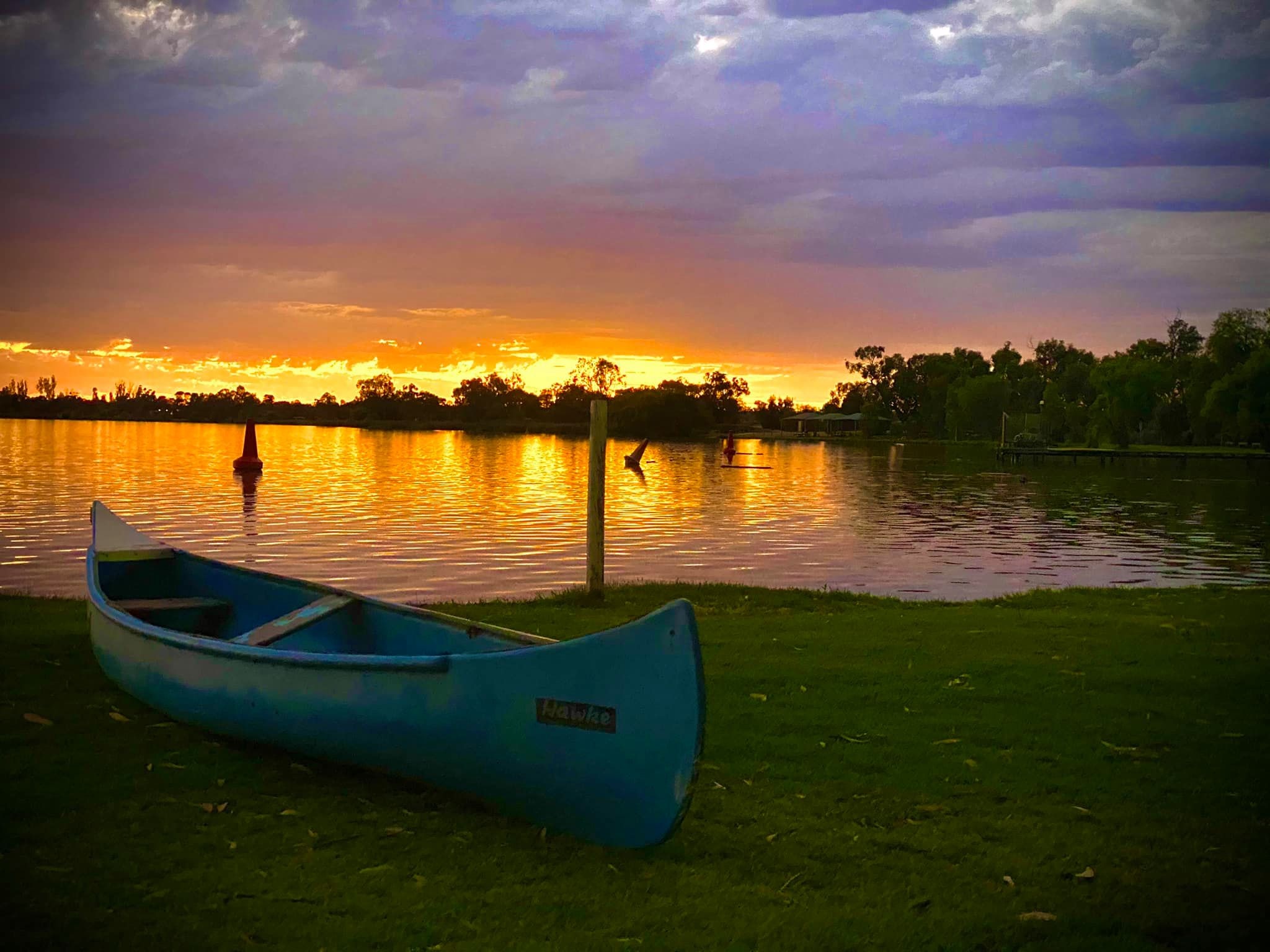 Canoe sitting on grass in front of sunset and lake