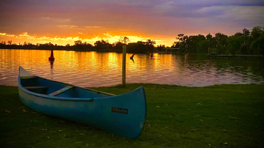 Canoe sitting on grass in front of sunset and lake