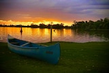Canoe sitting on grass in front of sunset and lake