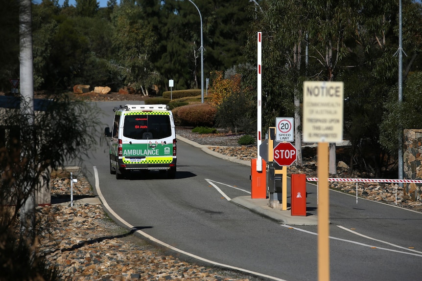 A wide shot of a St John Ambulance driving through security gates and up a road.
