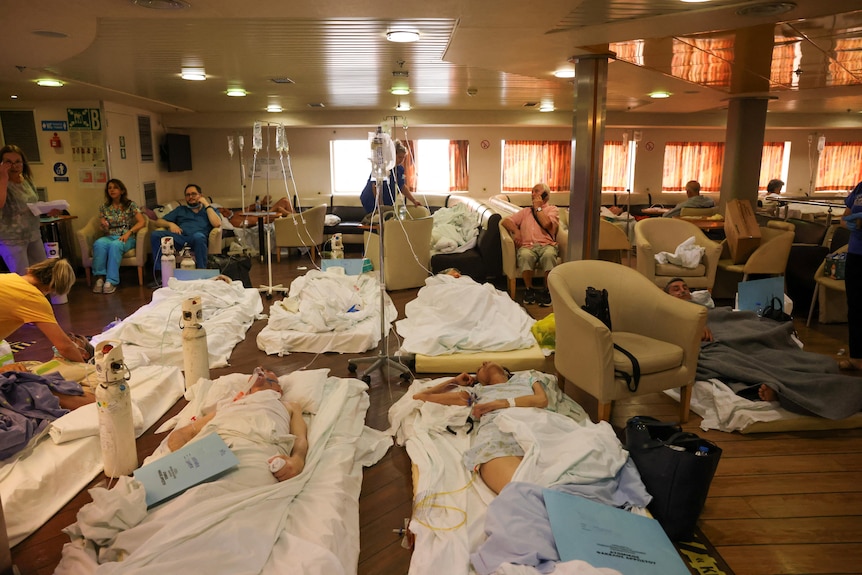 Hospital patients lying on mattresses on the floor inside a ferry with IV drips attached to them