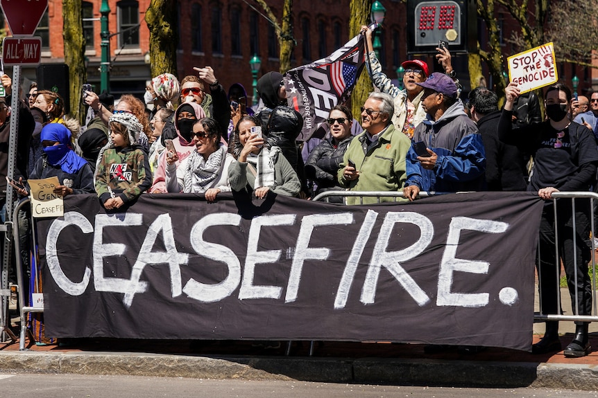 A group of protesters stand behind a 'ceasefire' sign 