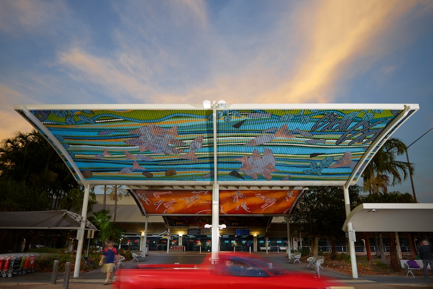 A large shade roof outside a terminal building and the underside is adorned with Aboriginal art.
