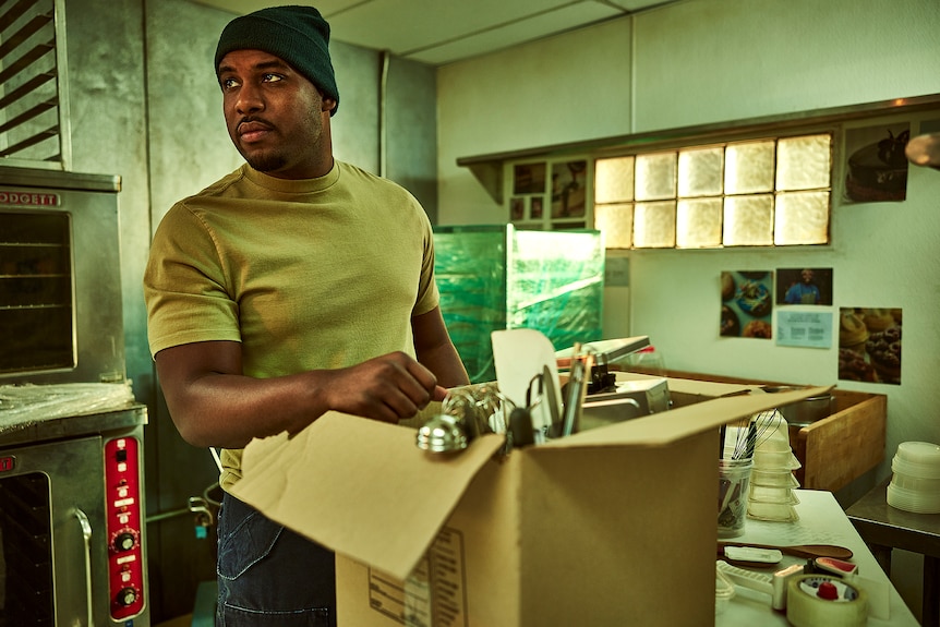 Marcus looks off screen as he unpacks a box in the kitchen.