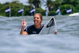 A female surfer sticks out her tongue and holds up her fingers after winning a competition