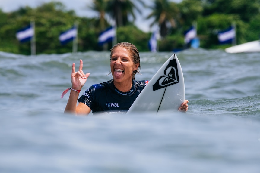 A female surfer sticks out her tongue and holds up her fingers after winning a competition