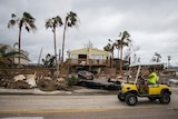 A man drives past debris scattered around the yards of houses.