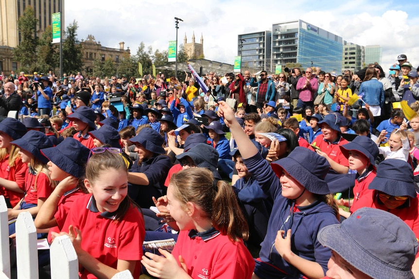 A crowd of school children and fans waving flags