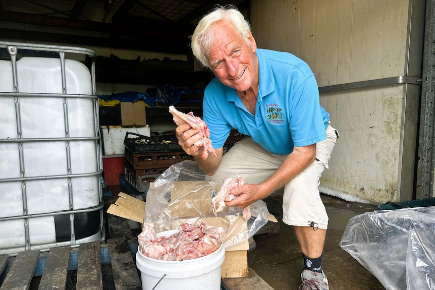 A man wearing a blue shirt holding a chicken carcasses from a white bucket.