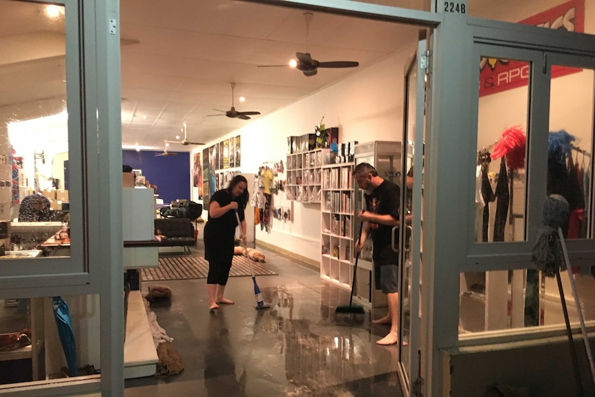 Owners of a games shop sweep out water that has flooded their business