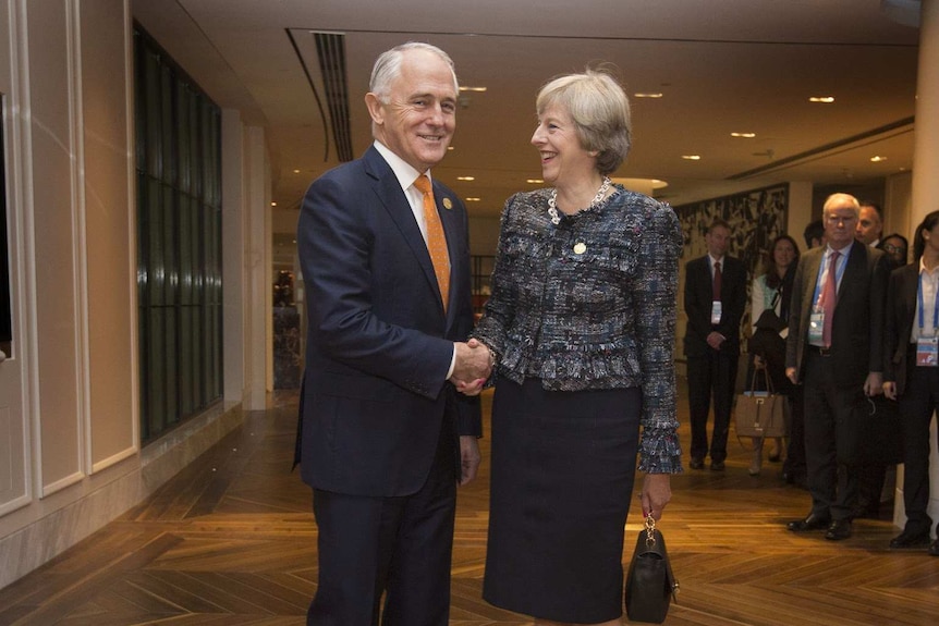 Malcolm Turnbull smiles and shakes hands with British Prime Minister Theresa May, who is laughing, at the G20 Summit.