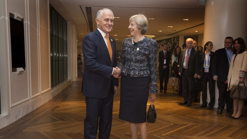 Malcolm Turnbull smiles and shakes hands with British Prime Minister Theresa May, who is laughing, at the G20 Summit.