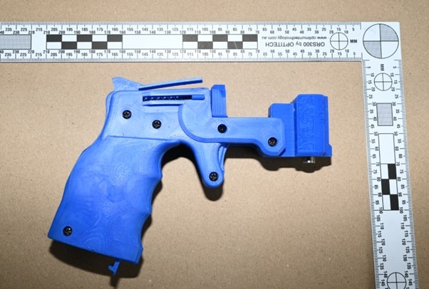 Una pistola azul impresa en 3D sobre una superficie plana junto a una regla.