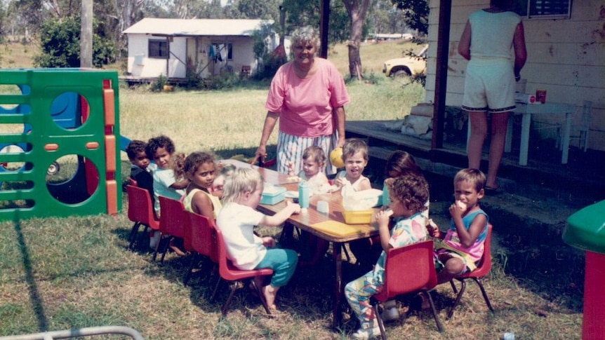 A group of Aboriginal children sit around a table at daycare with their teacher.