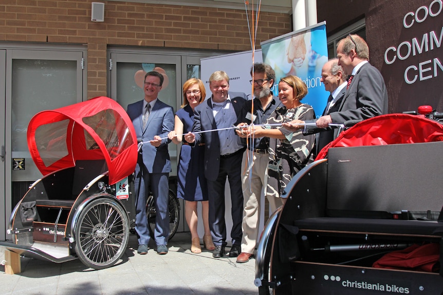 Women surrounded by ministers and Danish Ambassador cutting a ribbon.