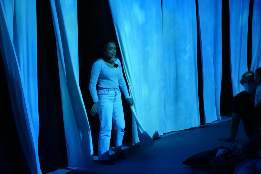 Silks blow in the wind on stage, and a performer stands amongst it