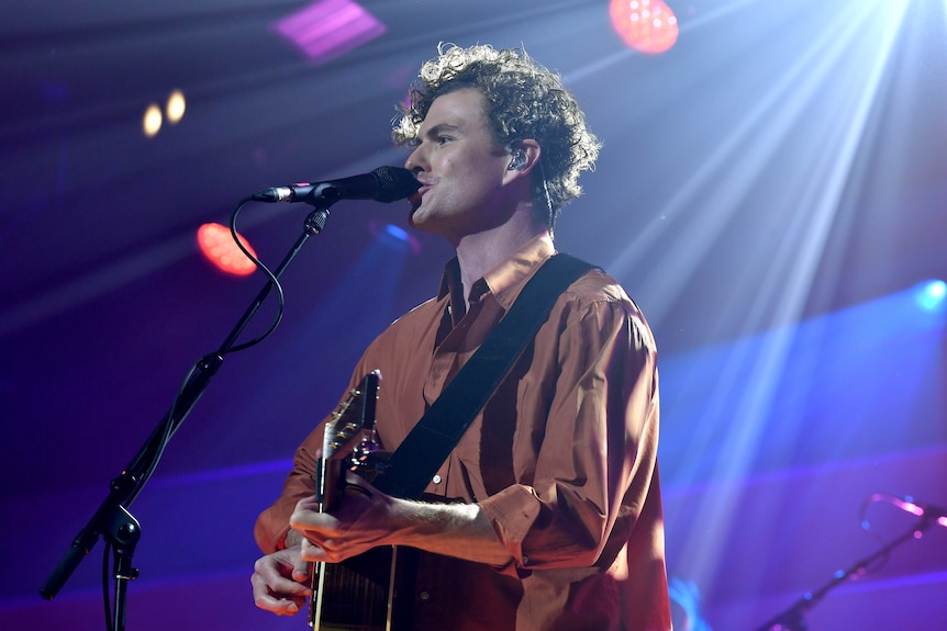 vance joy sings into microphone and plays guitar on stage