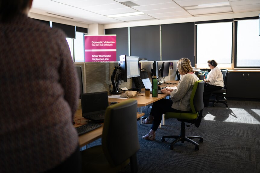 Staff sit in an office with a sign nearby for the domestic violence hotline