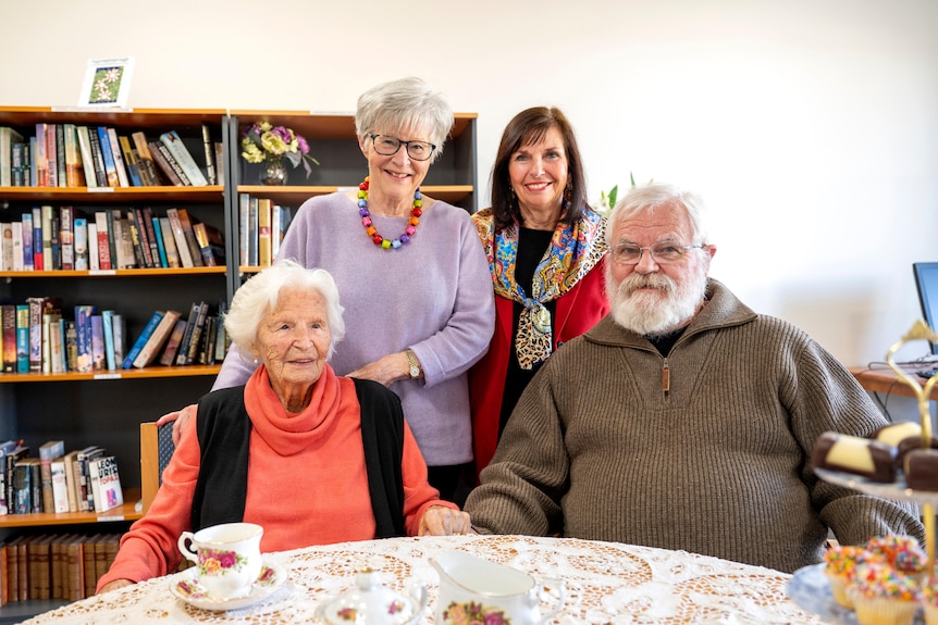 An elderly woman sitting at a table with her two daughters and her son. 