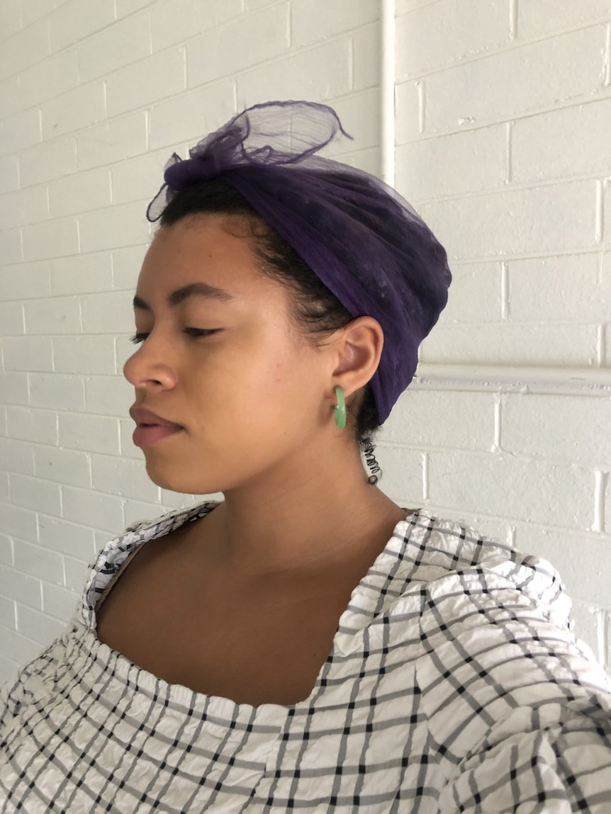 Portrait of journalist Yasmin Jeffery wearing a purple chiffon head wrap and green hoop earrings.