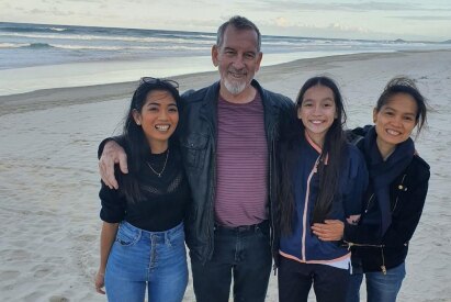 Bernard standing with his wife and daughters on the beach