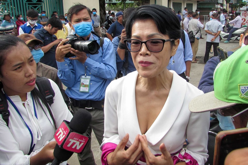 A woman in a white blazer dress gestures as she speaks to media in Cambodia outside court.