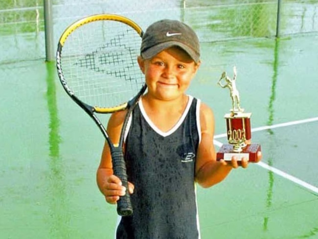 A little girl smiles as she holds up a trophy.