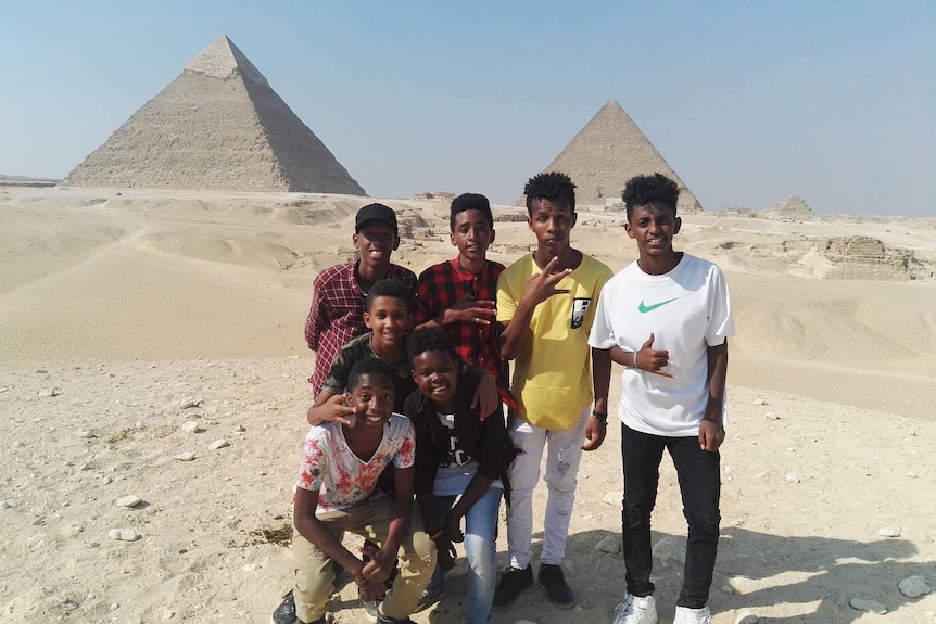 A group of seven boys stand together in front of two pyramids