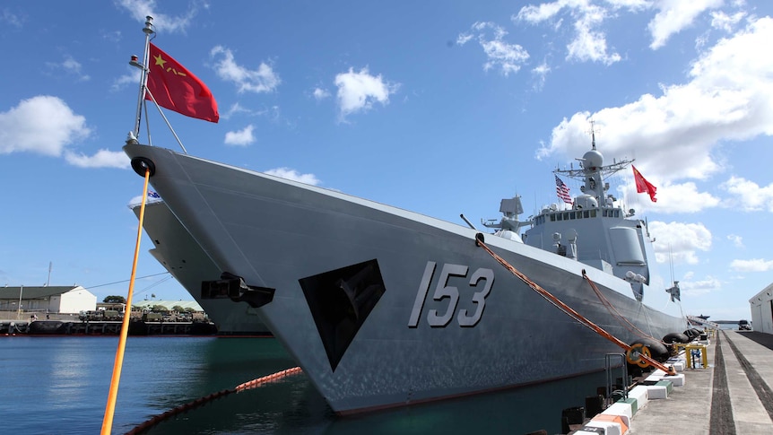 A Chinese Navy destroyer, with the Chinese flag waving at the front, can be seen tied to a dock.