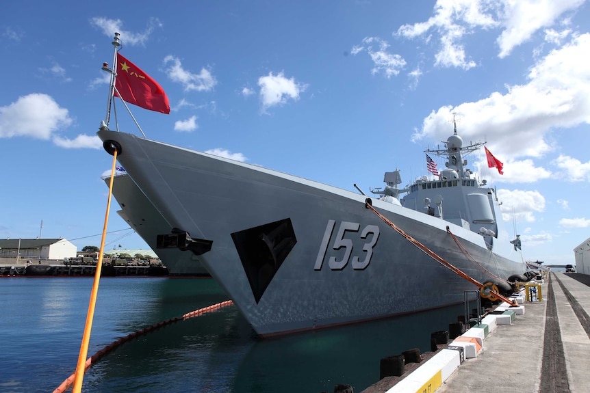 A Chinese Navy destroyer, with the Chinese flag waving at the front, can be seen tied to a dock.