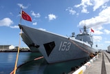 A Chinese Navy destroyer, with the Chinese flag waving at the front, can be seen tied to a dock.