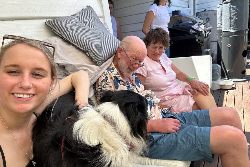 A man sits on a couch with his daughter, wife and dog