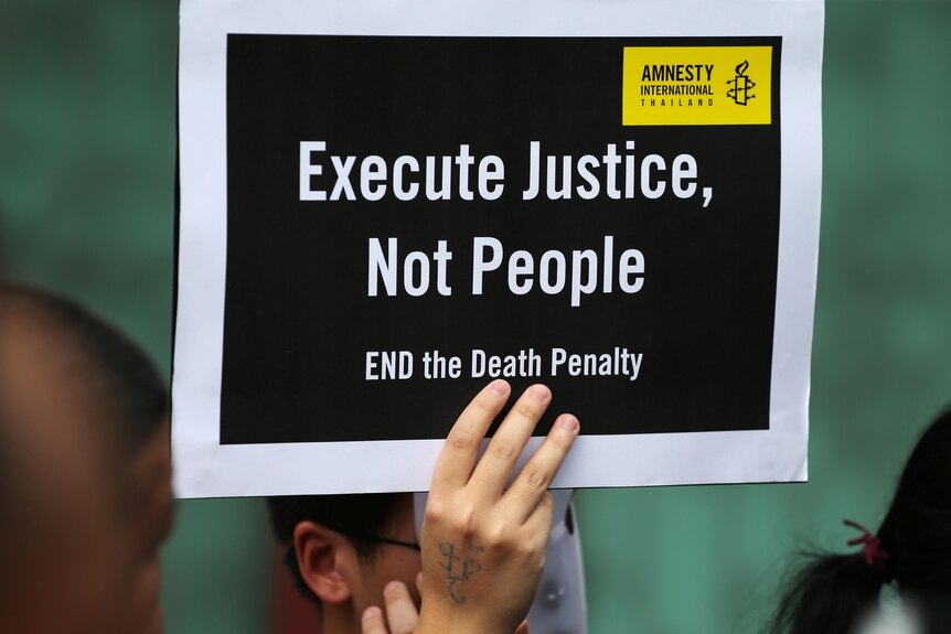 A hand a holds up a sign which reads "Execute Justice, Not People."