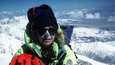 Brigitte Muir with white zinc or her face, sunglasses, beanie and snow clothing, on a snow-capped peak with mountain surrounds.
