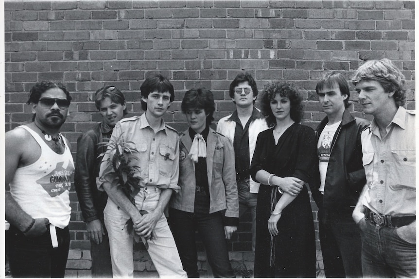 A band poses for a photo against a brick wall.