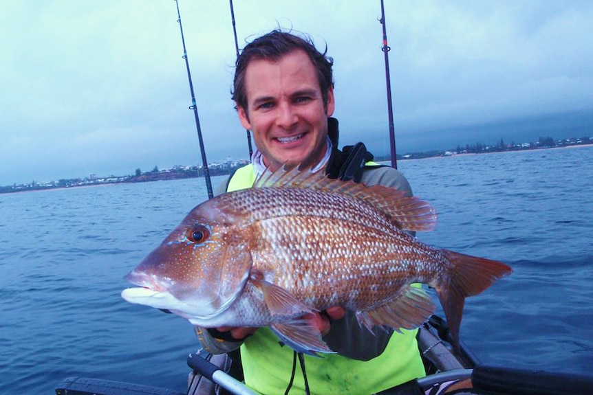 Kyle Roberts smiles as he holds a fish he caught while kayaking in the ocean off the Sunshine Coast.