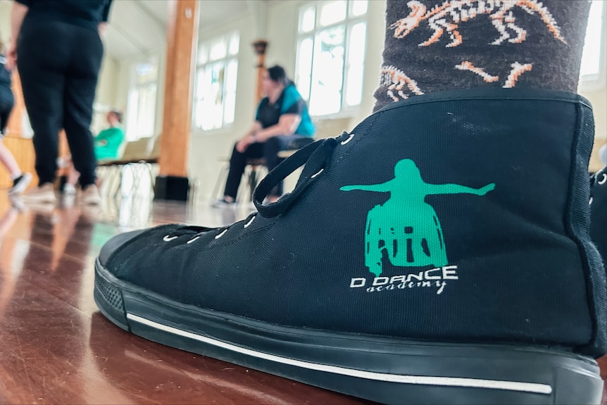 A close up picture of a canvas shoe with a logo of a figure dancing in a wheelchair