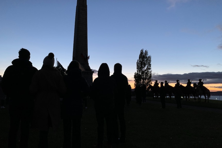People and horses gather in the dark at a cenotaph