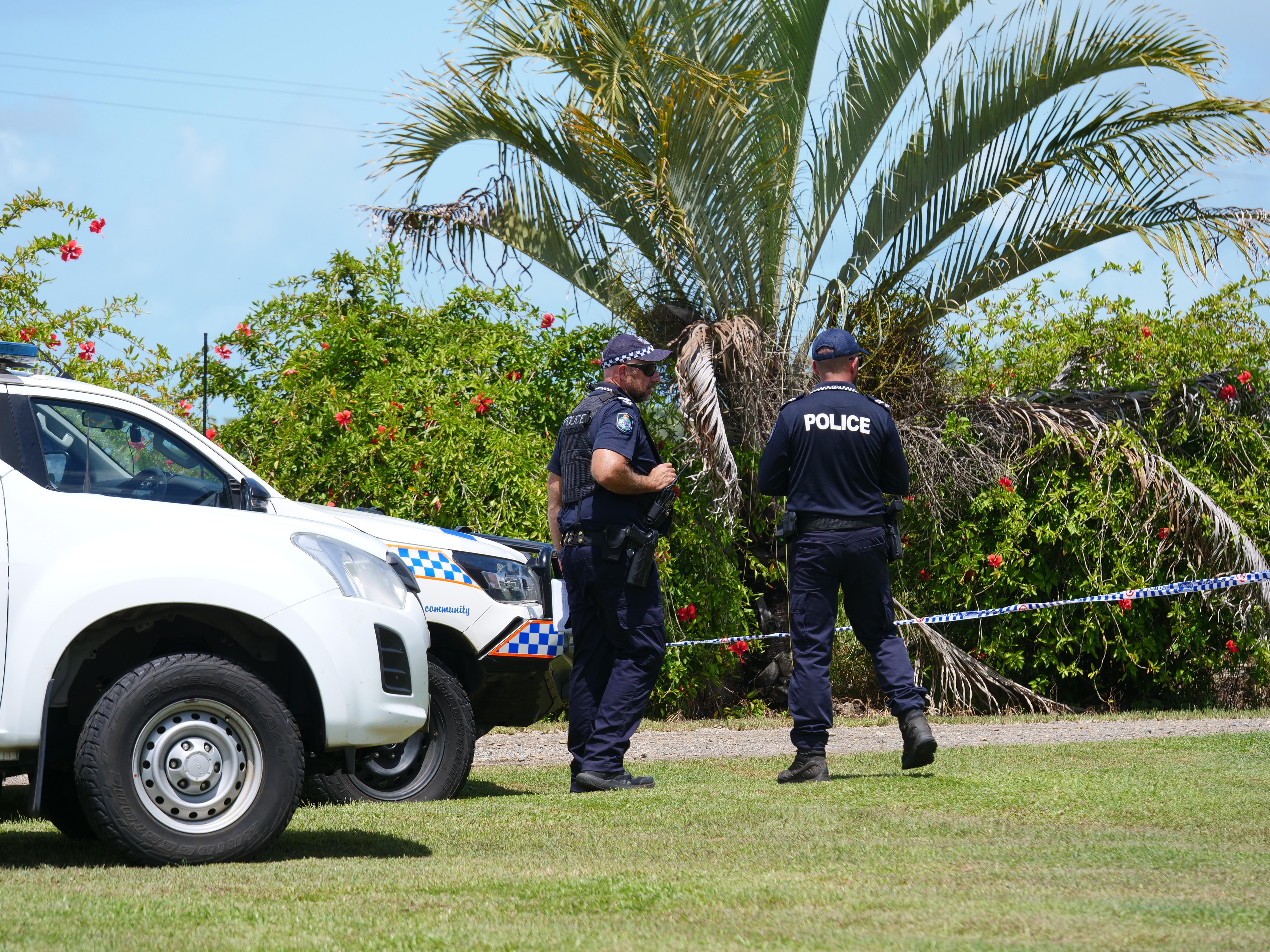 Police officers standing next to cars, with tropical plants visible behind