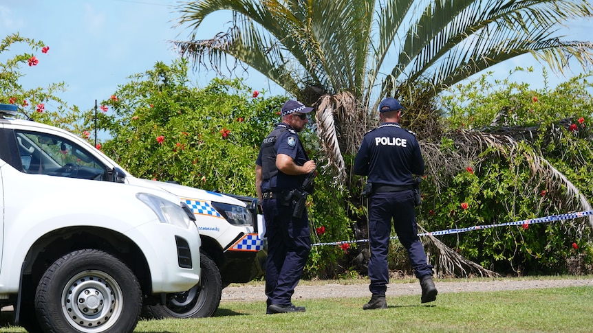 Police officers standing next to cars, with tropical plants visible behind