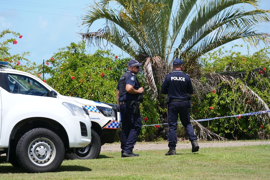 Police officers standing next to cars, with tropical plants visible behind