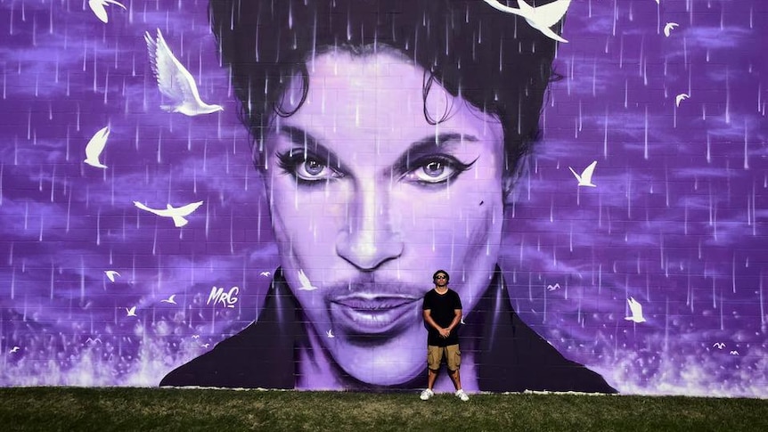 Graham Hoete poses in front of his Prince mural