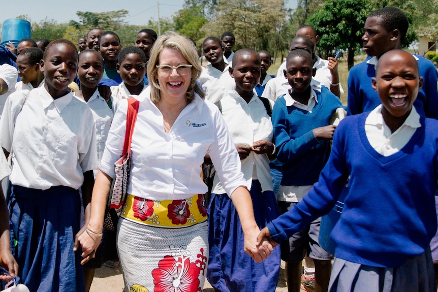 A blonde haired woman holds the hands of African school children