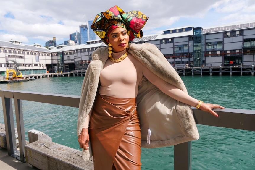 A finely-dressed woman with a fur coat over her soliers and a vibrant headwrap. 